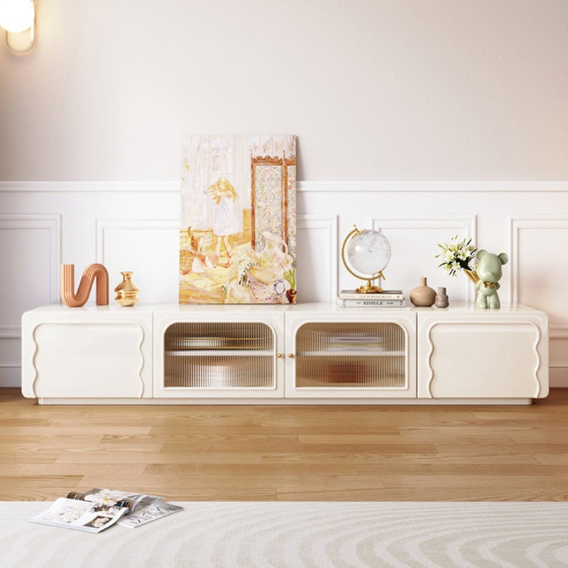 A white, small-sized Vibrate TV stand with fluted glass panels and golden knobs, along with push-to-open doors. It is placed in a room with decorative items on top and against a light-colored wall.