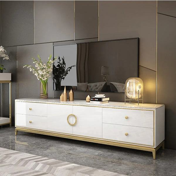 A white Vivian TV stand with a golden finish features four drawers and two doors, placed in a modern living room setting with a mirrored wall and contemporary decor.