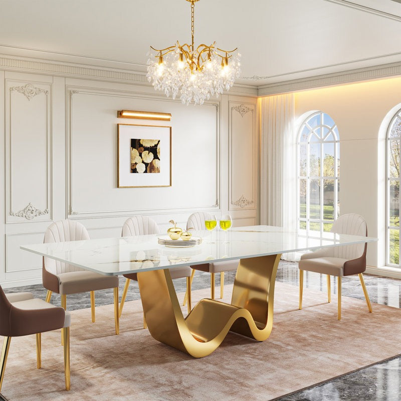An elegant 8-seater dining table set with a white marble top and golden powder-coated stainless steel W-shaped base, accompanied by eight high-back chairs with brown leatherette upholstery and golden metal legs, positioned in a luxurious dining room.