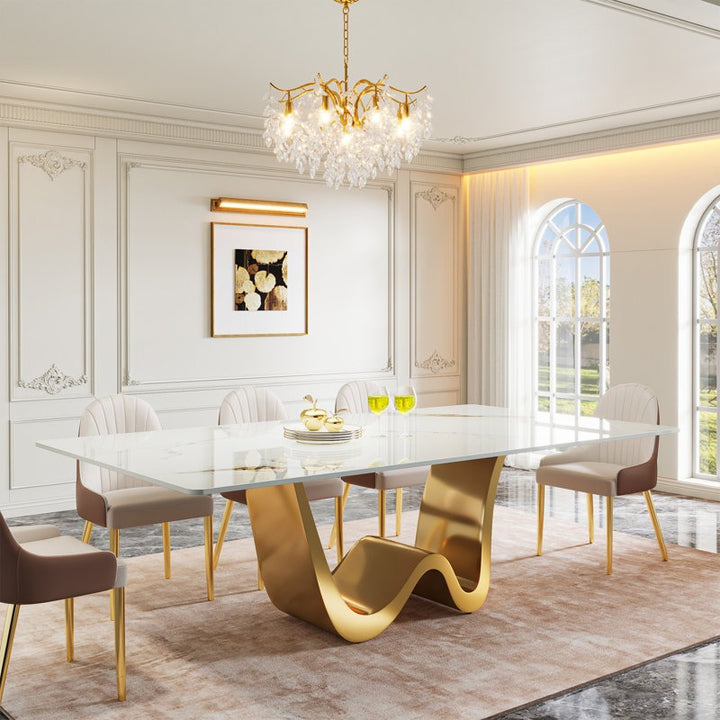 An elegant 8-seater dining table set with a white marble top and golden powder-coated stainless steel W-shaped base, accompanied by eight high-back chairs with brown leatherette upholstery and golden metal legs, positioned in a luxurious dining room.