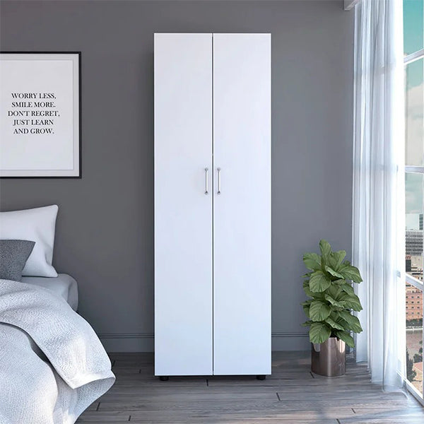 A white 2-door wardrobe with silver metal handles, placed in a bedroom setting with a plant to the side and a bed in the background.