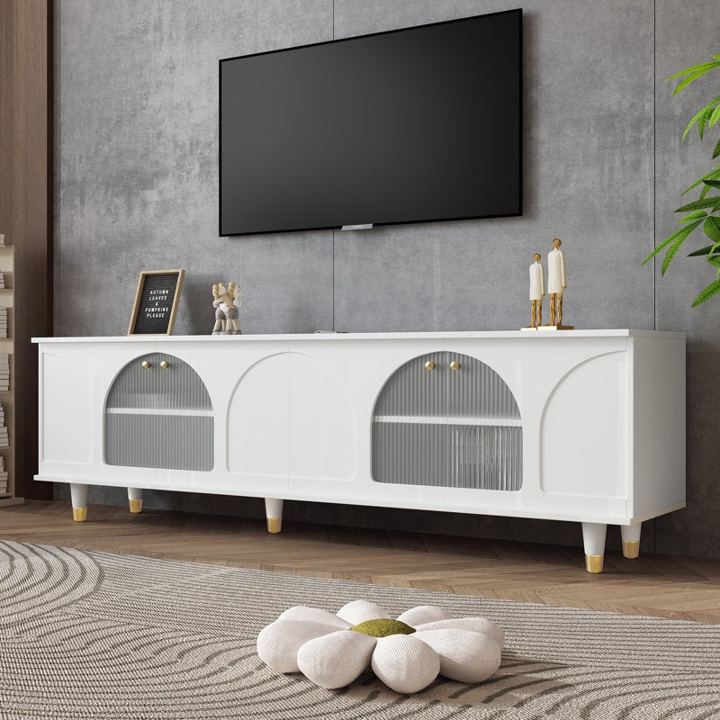 A white TV stand with fluted glass doors and golden accents, mounted on white-gold legs. A television and decorative items are placed on top, set against a minimalist interior background.