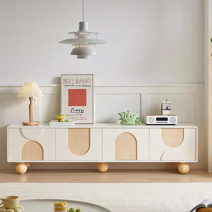 A white Brunzy TV stand with solid wood ball legs, featuring cut-outs in a different wood tone and spherical decorations on top.