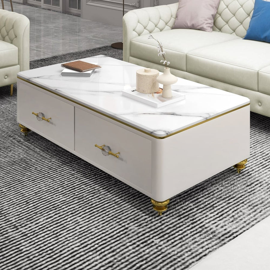 A modern neoclassical white coffee table with a marble top, gold trim, and four drawers, placed on a striped rug.