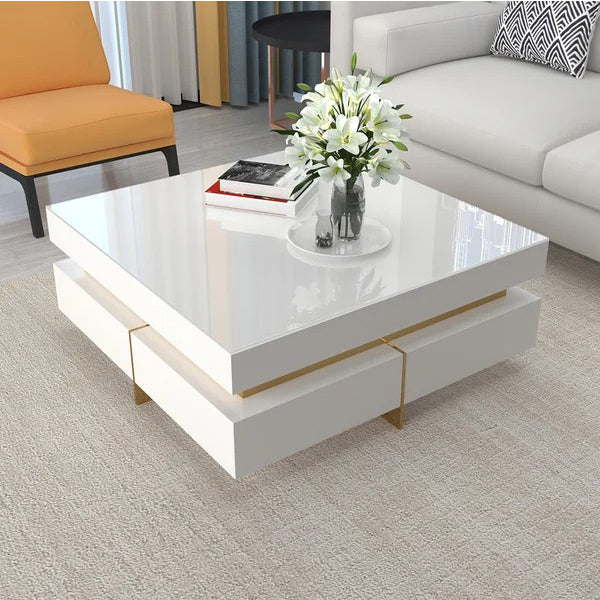 A white rectangular coffee table with metal golden legs, positioned on a rug in a living room setting. The table has a shiny surface and a decorative vase with flowers on top.