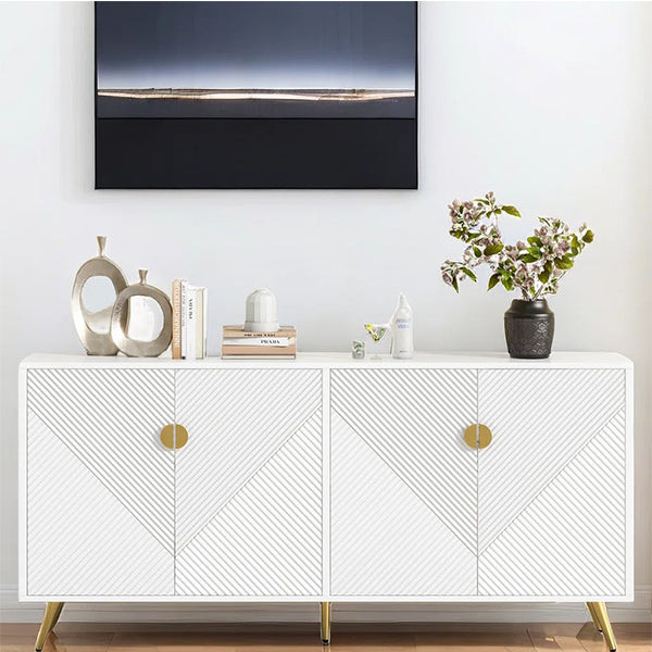 A white sideboard with geometric patterned doors and gold metal legs, featuring an abstract painting above it and decorative items like a plant and bottles on it.