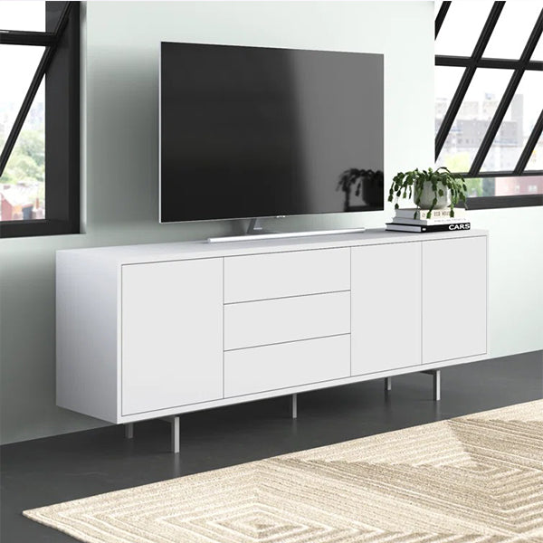 A large white sideboard and cabinet with metal legs, featuring three doors and a flat surface, placed in a room with a flat-screen TV on top and a rug on the floor.