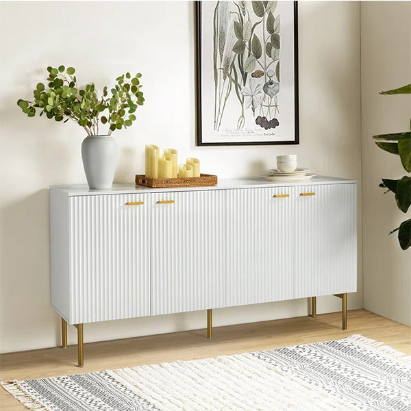 A small white sideboard with gold-colored handles and a geometric pattern on the front, placed in a room with a potted plant, candles, and a framed abstract picture on the wall.