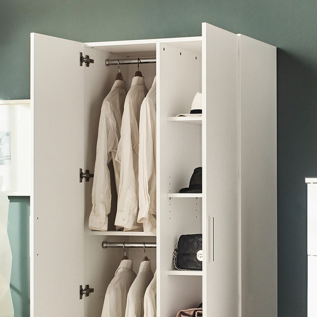 White 2-door wardrobe with clothes and bags inside against a gray wall